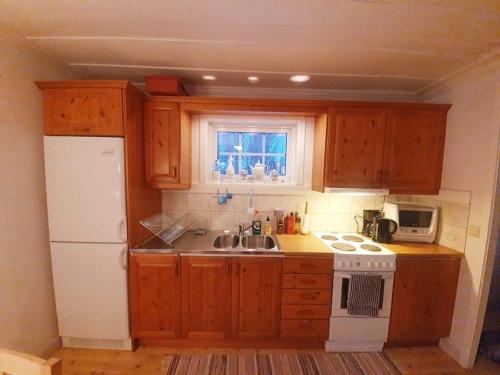 uma pequena cozinha com armários de madeira e um frigorífico branco em Guesthouse em Öjebyn