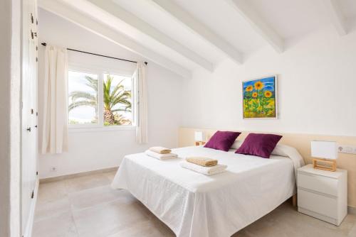 a white bedroom with two beds and a window at Villa BiniRe in Binibeca