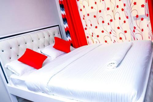 a white bed with two red pillows on it at Maven Sparkles Furnished Apartments in Kiambu