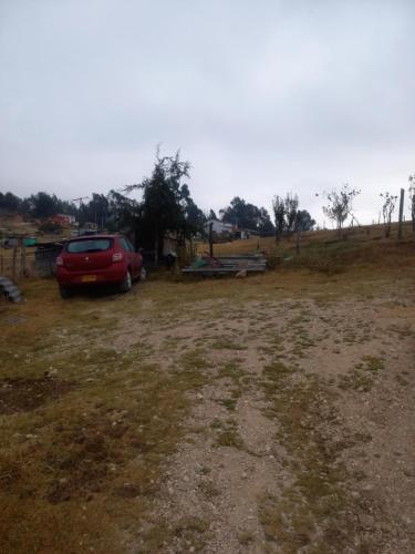 a red car parked in a dirt field at Cabaña Sueños Dorados in Guatavita