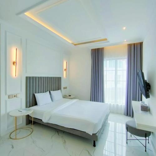 a white bedroom with a large bed and a television at Kala Hotel Semarang in Jomblang