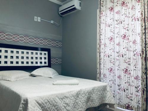 1 dormitorio con 1 cama con sábanas blancas y cortina en Residencia da Kel, en Bombinhas
