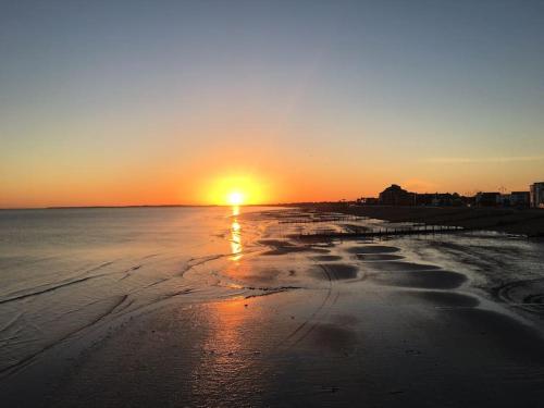 a sunset on a beach with the sun setting at Stay in our beautiful 1850’s Coastguards Cottage. in Felpham