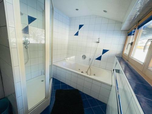 La salle de bains est pourvue d'une baignoire et d'une douche avec du carrelage bleu. dans l'établissement Hugo - der Bodenständige - Huusa im Bregenzerwald, à Rehmen