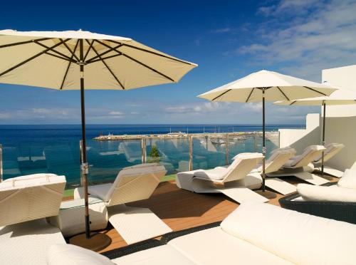 a pool with white chairs and umbrellas and the ocean at Boutique Hotel H10 Big Sur - Adults Only in Los Cristianos