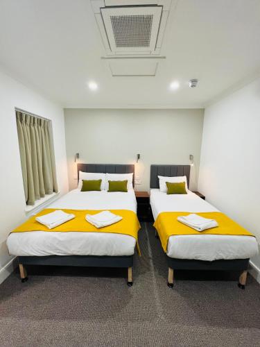 two beds in a room with yellow sheets at Park Avenue Bayswater Inn Hyde Park in London