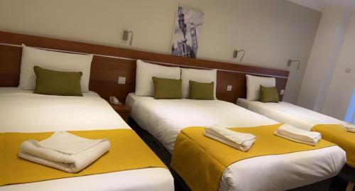 three beds in a hotel room with towels on them at Park Avenue Bayswater Inn Hyde Park in London