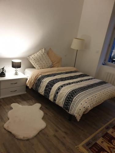een slaapkamer met een bed en een tafel met een lamp bij Appartement COSY et chaleureux in Lons-le-Saunier