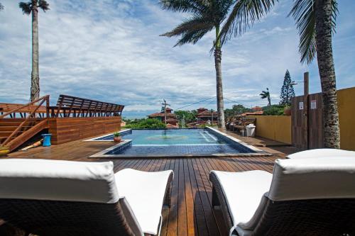 a deck with chairs and a swimming pool with palm trees at Hotel Pousada Casacolina in Búzios