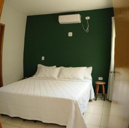 a bedroom with a white bed with a green wall at Casa no centro com 4 quartos e ar condicionado in São João Batista do Glória