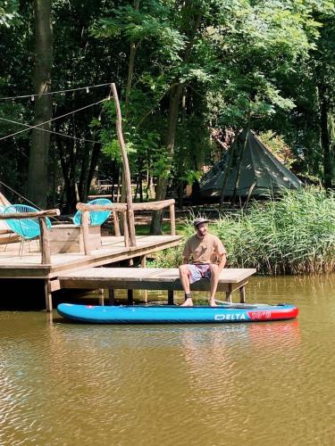 a man sitting on a bench next to a paddle board in the water at ASILI DELUXE - Zebra in Lichtaart