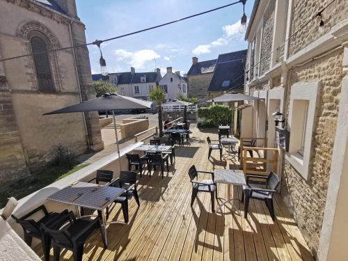 a patio area with tables, chairs and umbrellas at Hôtel Restaurant Le Mulberry Arromanches in Arromanches-les-Bains