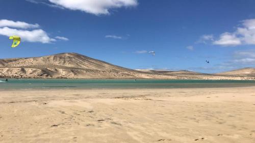 a person flying a kite on a beach with mountains in the background at Rio Sol - Oasis de Privacidad in Costa Calma