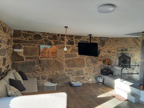 un soggiorno con parete in pietra, divano e TV di Casita de norma a Camariñas