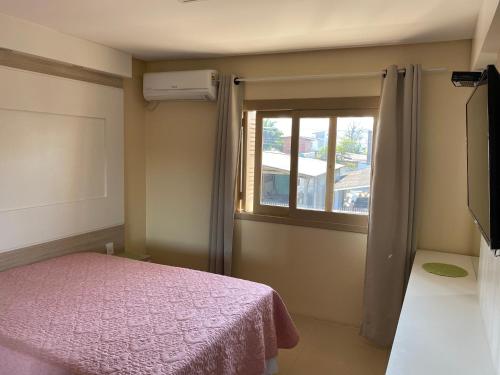 1 dormitorio con cama rosa y ventana en Apartamento Maria Helena, en Torres