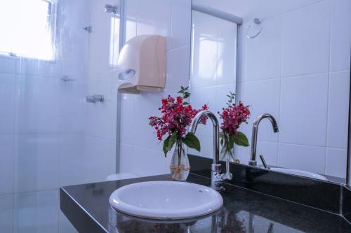 a bathroom with a sink with a toilet and flowers at Hotel Bandeirantes in Cachoeira do Campo