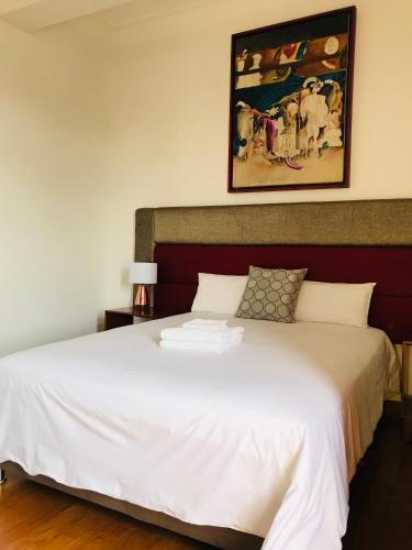 a bedroom with a white bed with a painting on the wall at Larq'a Park Rooms in Lima