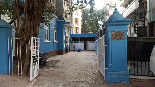 a blue gate in front of a building with a tree at Bentleys Hotel in Mumbai