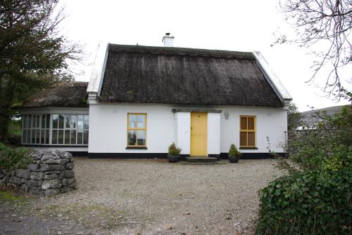 a white house with a black roof and yellow door at Ballyvaughan Cottages in Ballyvaughan