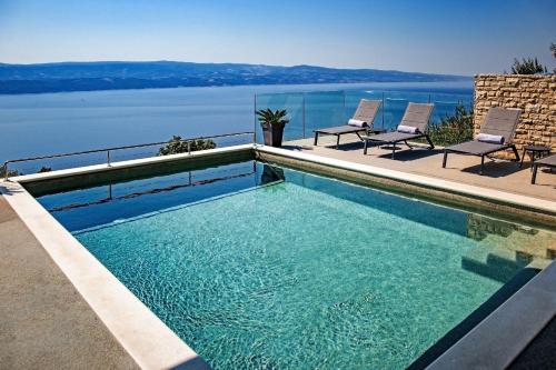 a swimming pool with chairs and a view of the water at Villa Dispet, sea view, pool, jacuzzi, sauna, cinema in Omiš
