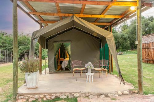 a tent with two chairs and a table in it at Schoemanshoek Glamping in Oudtshoorn