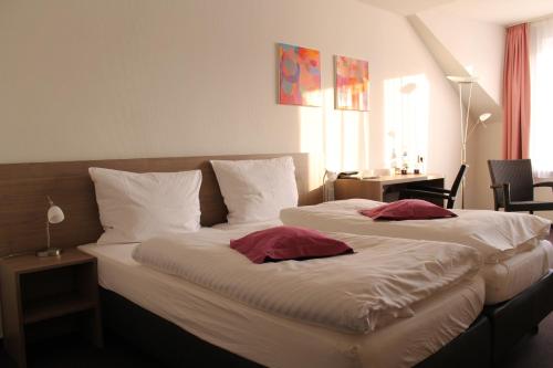 a bedroom with two beds with white sheets and red pillows at RheinHotel ARTE in Remagen