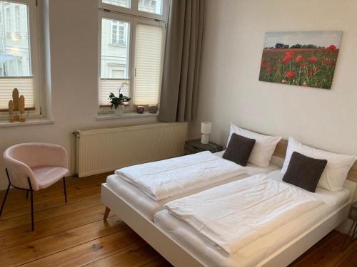 a bedroom with a white bed with a chair and windows at Das BilderbuchCafe - Pension Markt 7 in Havelberg