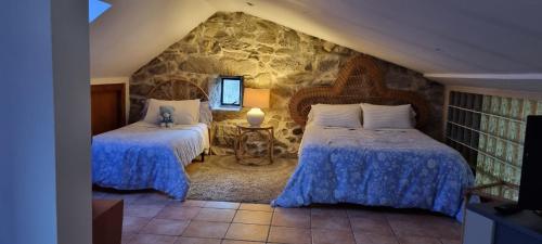 a bedroom with two beds and a stone wall at Casa do Crego in Vilaboa