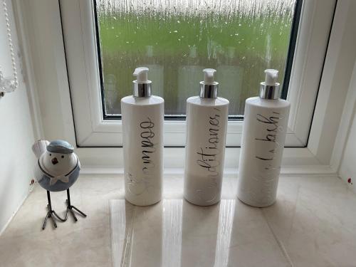 three white shampoo bottles sitting on a window sill at Anvil Cottage in Mold