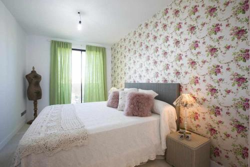 1 dormitorio con cama blanca y papel pintado con motivos florales en Beachfront Es Turo, en Colonia de Sant Jordi