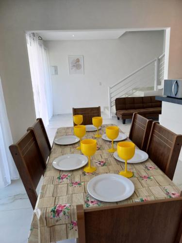 a wooden table with plates and yellow wine glasses at VIA CARNEIROS DUPLEX in Praia dos Carneiros