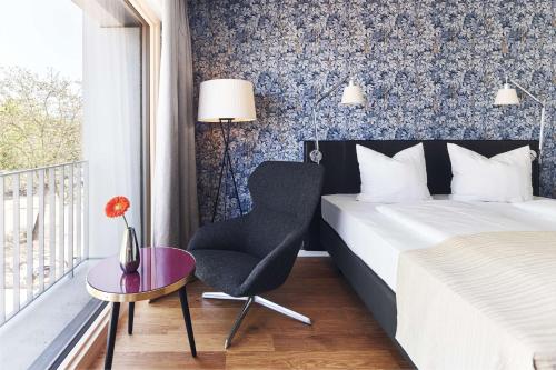 a bedroom with a bed and a chair and a window at Parkhotel Heilbronn in Heilbronn