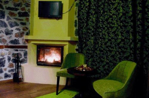 a living room with two green chairs and a fireplace at Gioras Hotel in Palaios Agios Athanasios