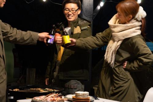 two people holding bottles of beer next to a table with food at SWEET VILLA TAKASAMA in Fujiyoshida