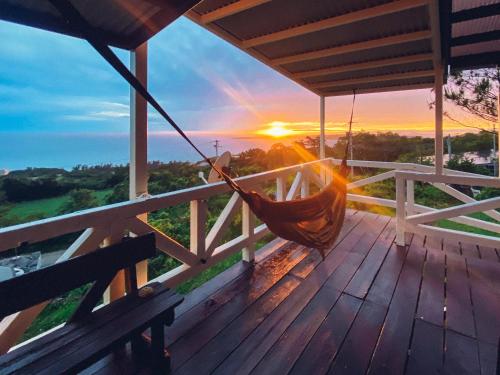 a hammock on the deck of a house with the sunset at PANORAMA Ocean View Cottage in Motobu