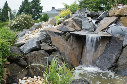 a waterfall in a garden with rocks at Maarberg Resort in Schalkenmehren