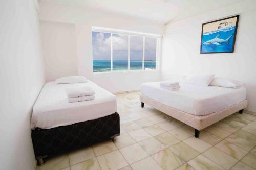 two beds in a white room with a window at Penthouse Barlovento para 19 personas in San Andrés
