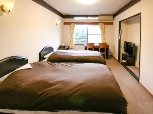 two beds in a room with a window and a television at Pension Kinrinko Toyonokuni in Yufuin