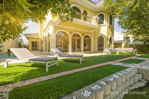 a house with a lawn with two lounge chairs in the yard at LUX - The Savoy Palm Villa in Dubai