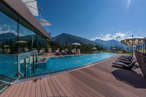 a beach with a pool, chairs, and a balcony at Hotel Albion Mountain Spa Resort Dolomites in Ortisei