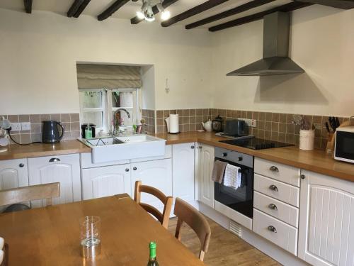 a kitchen with white cabinets and a wooden table at 200 year old Gardener's cottage, Mid Wales in Llanidloes