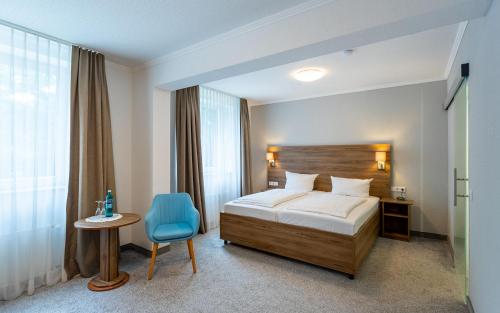 a bedroom with a bed and a table and a blue chair at Waldhotel Eskeshof in Wuppertal