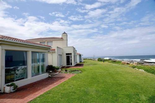 a house with a grass yard next to the ocean at Whales & Waves in Hermanus