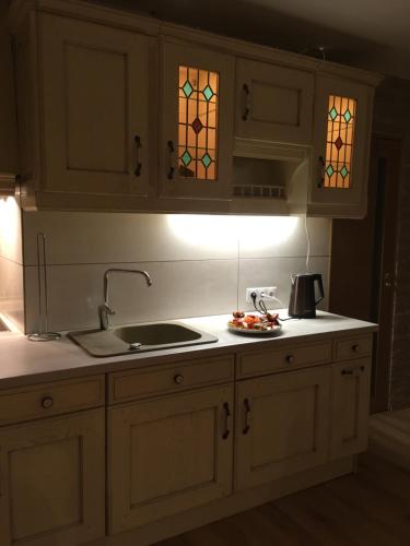 eine Küche mit weißen Schränken, einem Waschbecken und Buntglasfenstern in der Unterkunft Apartamenti MĀRA in Madona