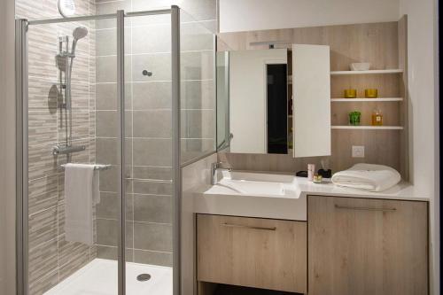uma casa de banho com um chuveiro, um lavatório e uma cabina de duche em vidro. em Domitys Les Raisins Bleus em Villiers-sur-Marne