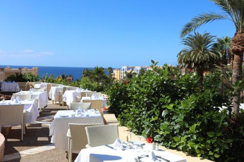 a restaurant with white tables and chairs and palm trees at Bahia Principe Sunlight Costa Adeje - All Inclusive in Adeje