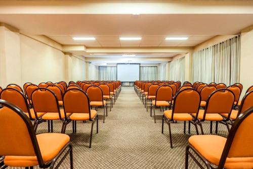 an empty conference room with orange chairs and a screen at Hotel Tannenhof in Joinville
