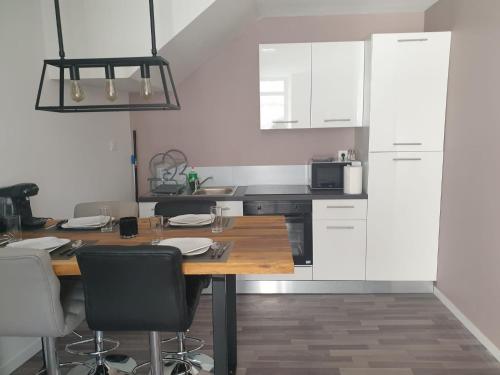 une cuisine avec une table en bois et des armoires blanches dans l'établissement Le bel'air appartement chaleureux et calme oyonnax, à Oyonnax