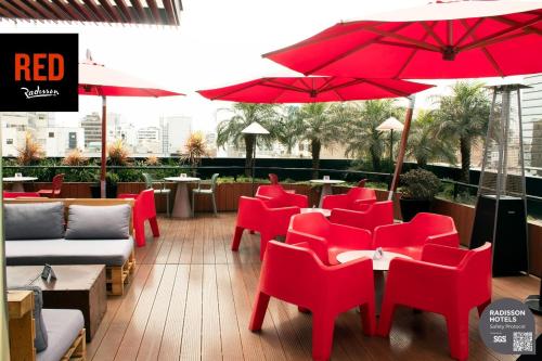 un restaurante con sillas rojas, mesas y sombrillas en Radisson RED Miraflores, en Lima
