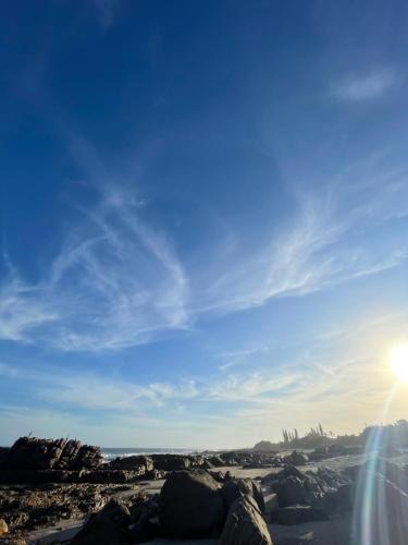 a beach with rocks and the sun in the sky at Casa da Flores Port Edward RSA in Port Edward